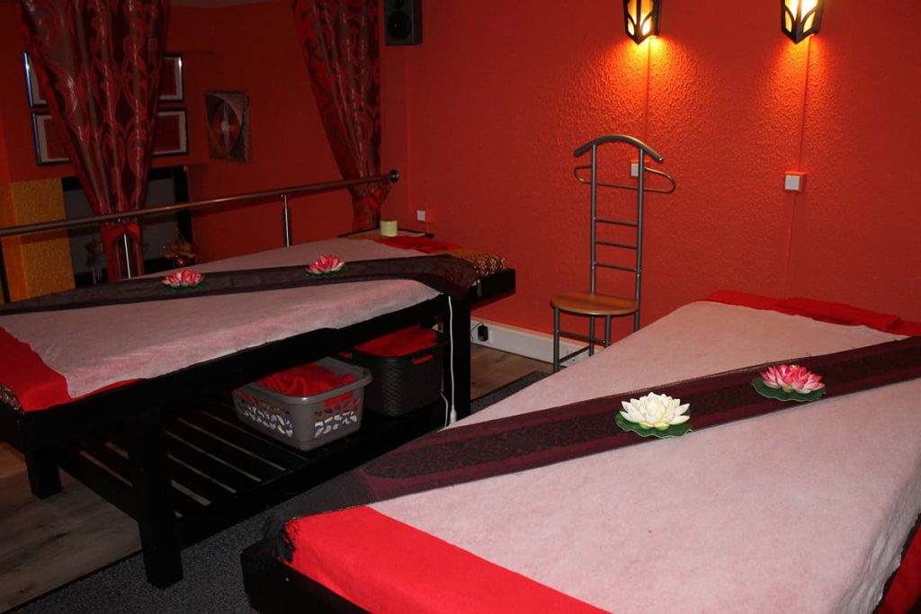 Blick aus dem oberen Bereich von Thai Life Massage Velbert, mit zwei Massage-Liegen, stimmungsvoll beleuchtet und geschmückt mit Lotusblumen, die eine beruhigende Atmosphäre unterstreichen.