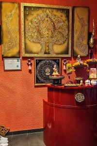Die Kasse von Thai Life Massage Velbert, umgeben von stilvollem Dekor und goldener Wandverzierung, die eine elegante und einladende Atmosphäre im Eingangsbereich schafft.