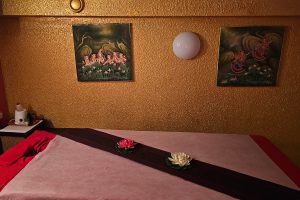 Massage-Liege von Thai Life Massage Velbert, platziert vor einer goldgestrichenen Wand, geschmückt mit schönen, gemalten Bildern, die eine entspannende und harmonische Atmosphäre schaffen.