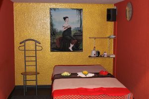 Nahaufnahme der Massage-Liege im unteren Bereich von Thai Life Massage Velbert, vor einer goldgestrichenen Wand, die von einem kunstvollen Gemälde geschmückt wird.