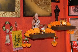 Nahaufnahme des Wanddekors bei Thai Life Massage Velbert, mit Buddha und weiteren traditionellen Figuren, einem kleinen Glas Alkohol als Opfergabe und Blumen, die dem Raum eine spirituelle Atmosphäre verleihen.